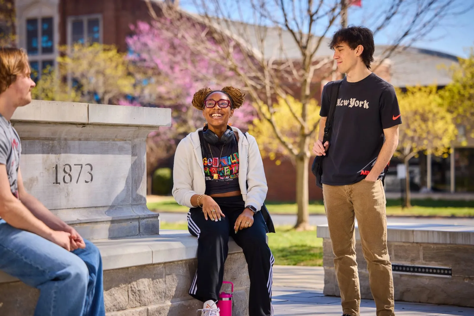 Three students talking beside the 1873 campus marker in spring